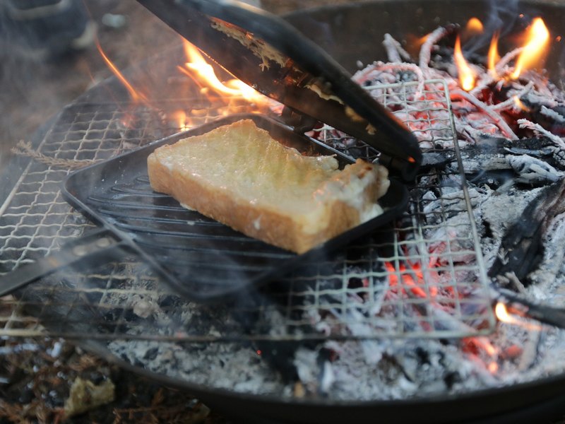 焚き火の上のホットサンドメーカーで焼かれるパン